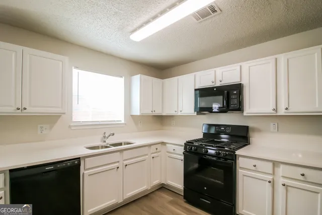 a kitchen with stainless steel appliances granite countertop white cabinets a sink and a window