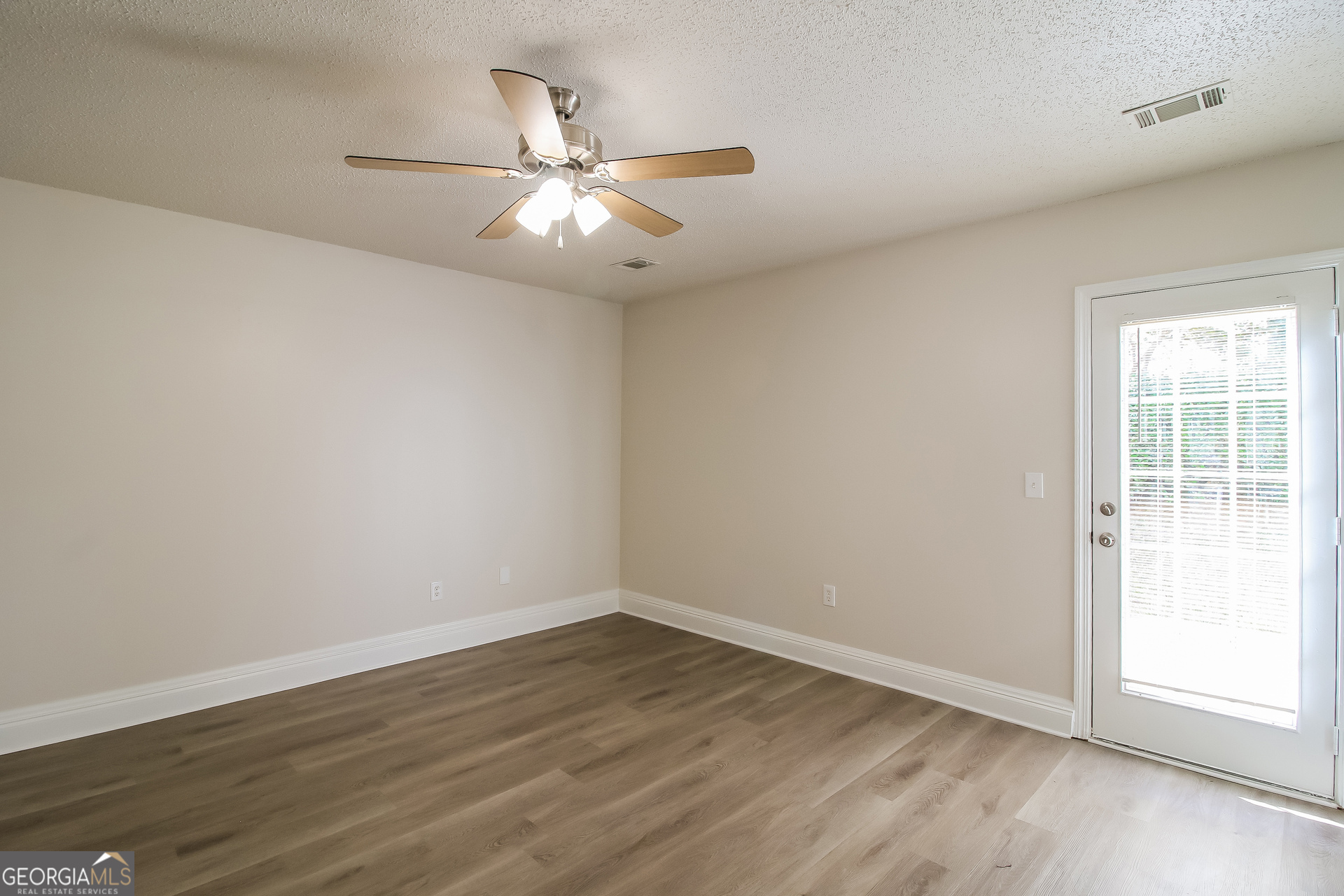 225 Colser Drive Covington, GA 30016 - Photo 7 of 17 an empty room with wooden floor fan and windows