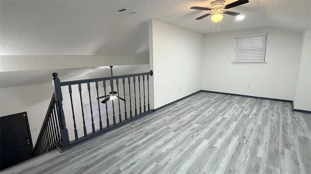 an empty room with wooden floor fan and windows