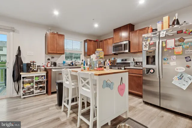 a kitchen with stainless steel appliances granite countertop a refrigerator a stove a sink dishwasher and a dining table with wooden floor