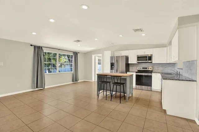 a kitchen with stainless steel appliances granite countertop a stove top oven a sink a dining table and chairs