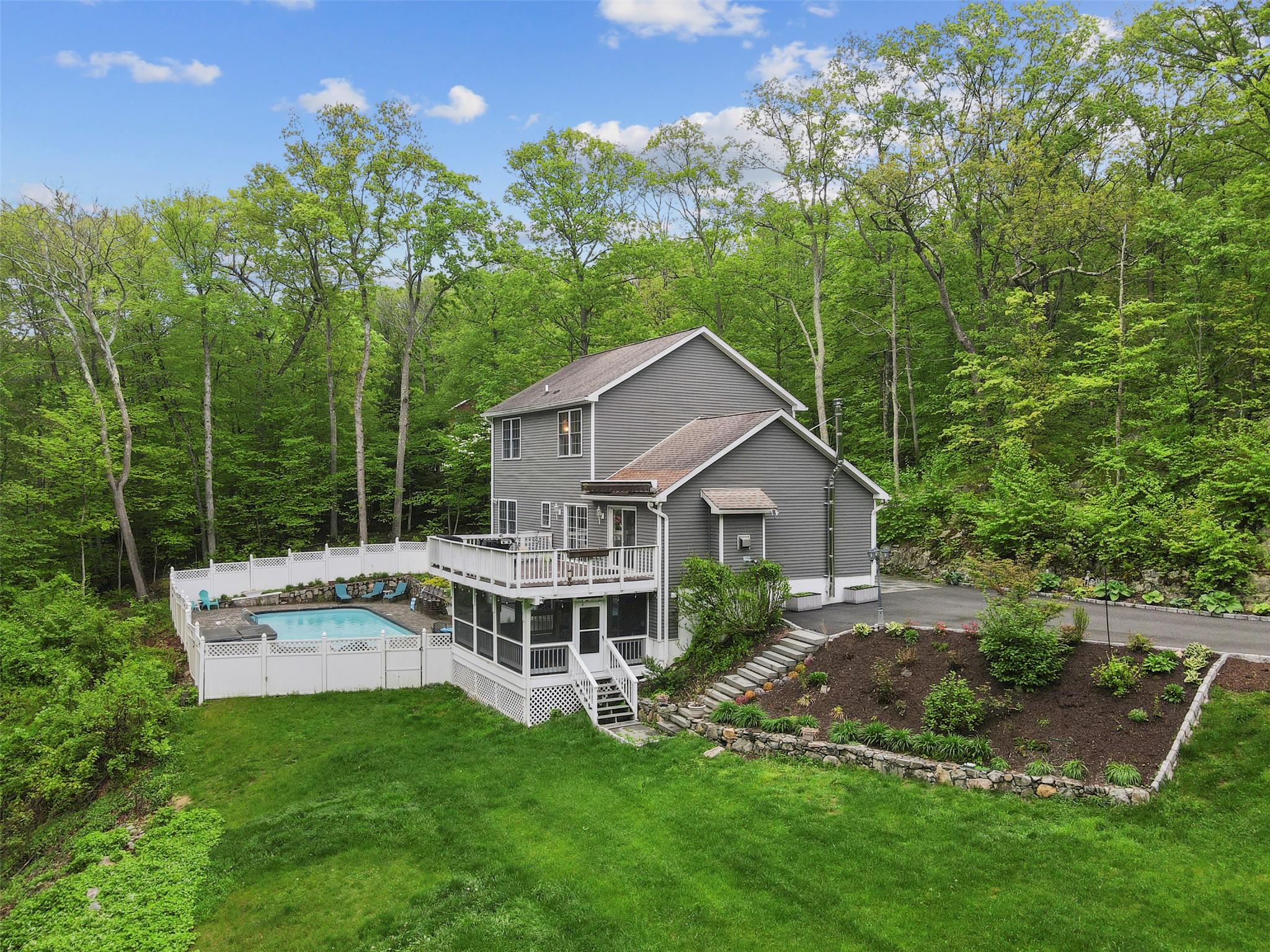Back of property featuring a deck, a view of trees, stairs, and a sunroom