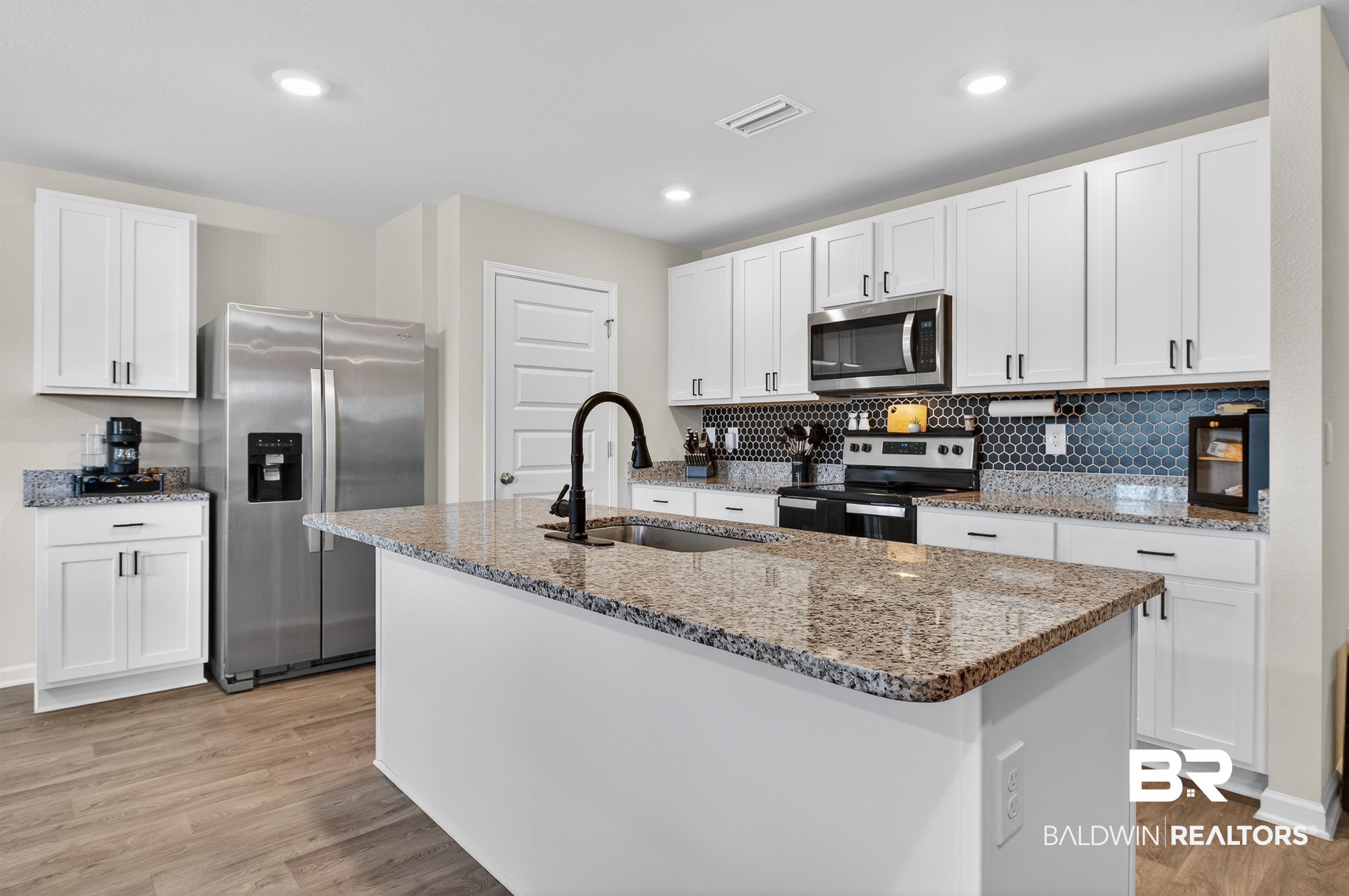 3213 Camino Real Loop Lillian, AL 36549 - Photo 29 of 61 Kitchen featuring a central island with a sink, white cabinetry, stainless steel appliances, speckled countertops, and a dark hexagonal tile backsplash