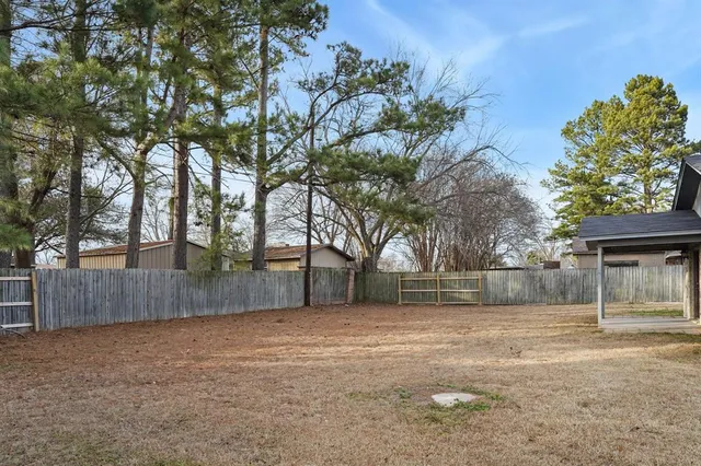 a backyard of a house with large trees and wooden fence