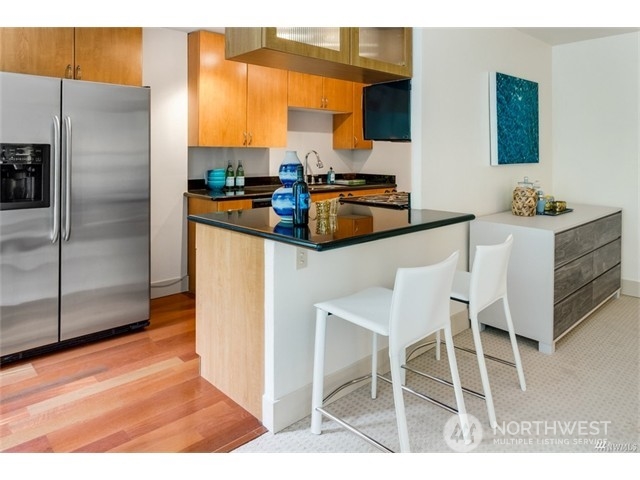1105 Spring Street, Unit 305 Seattle, WA 98104 - Photo 21 of 25 a kitchen with stainless steel appliances kitchen island granite countertop a table chairs microwave and sink