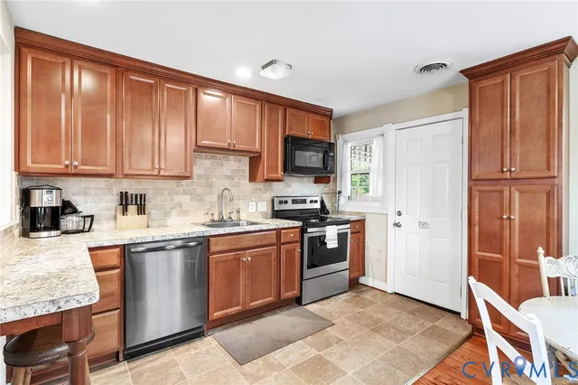 a kitchen with stainless steel appliances granite countertop a stove top oven a sink dishwasher and a refrigerator with wooden cabinets