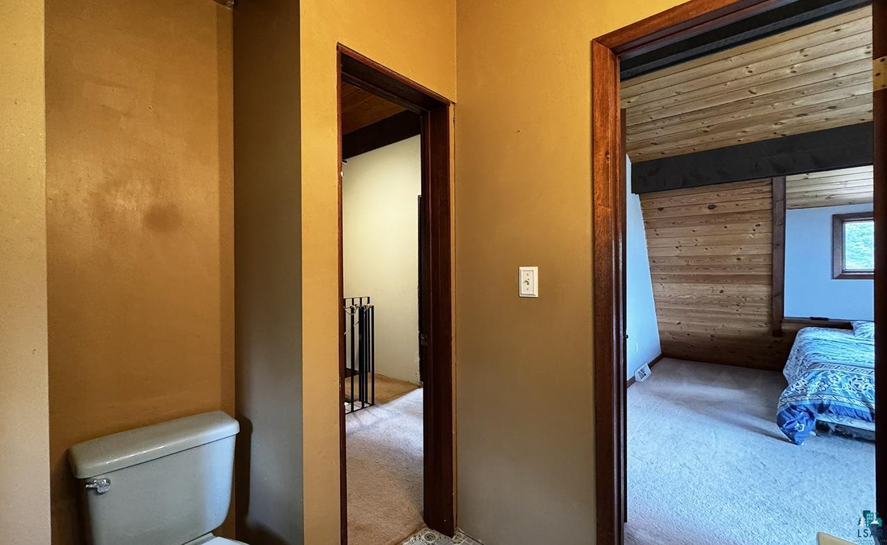 9289 Heino Road Angora, MN 55703 - Photo 17 of 37 Interior hallway featuring a toilet with an adjacent doorway opening to a room with wood-finish paneling and wood-finish ceiling