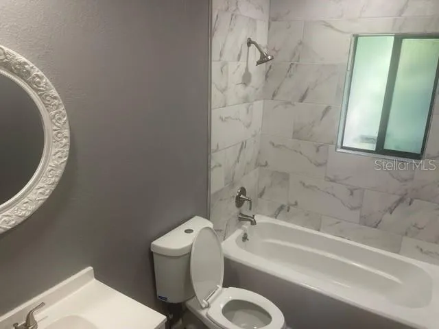 a bathroom with a granite countertop bathtub sink vanity mirror and toilet