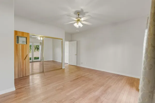 a view of an empty room with wooden floor and a ceiling fan
