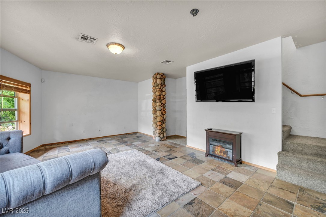 4137 Matterhorn Way Las Vegas, NV 89124 - Photo 62 of 75 Living room with a glass covered fireplace, stone tile flooring, stairs, and a textured ceiling