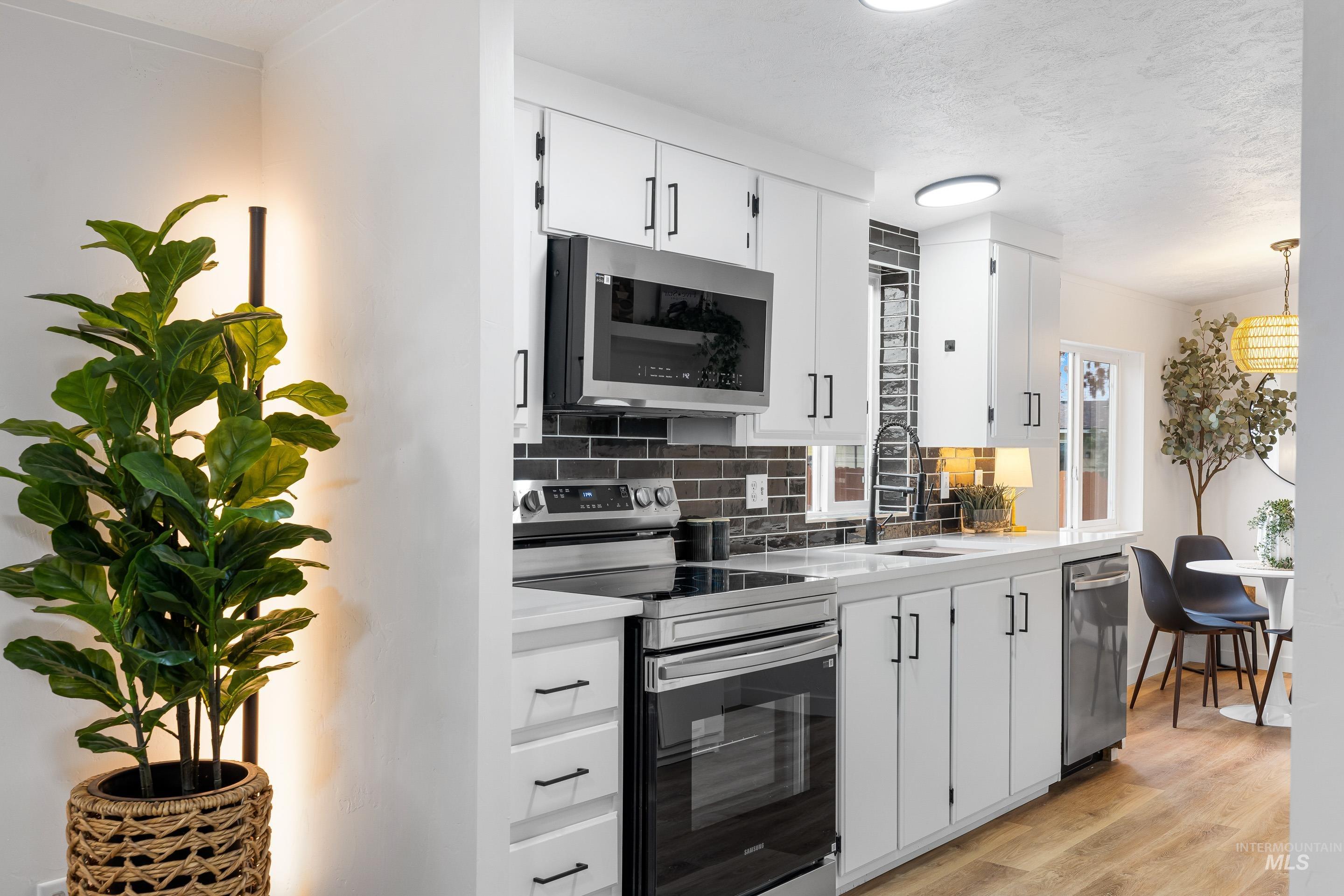 10014 Dewitt Lane Boise, ID 83704 - Photo 17 of 50 Kitchen with appliances with stainless steel finishes, tasteful backsplash, white cabinetry, light wood-style floors, and a textured ceiling