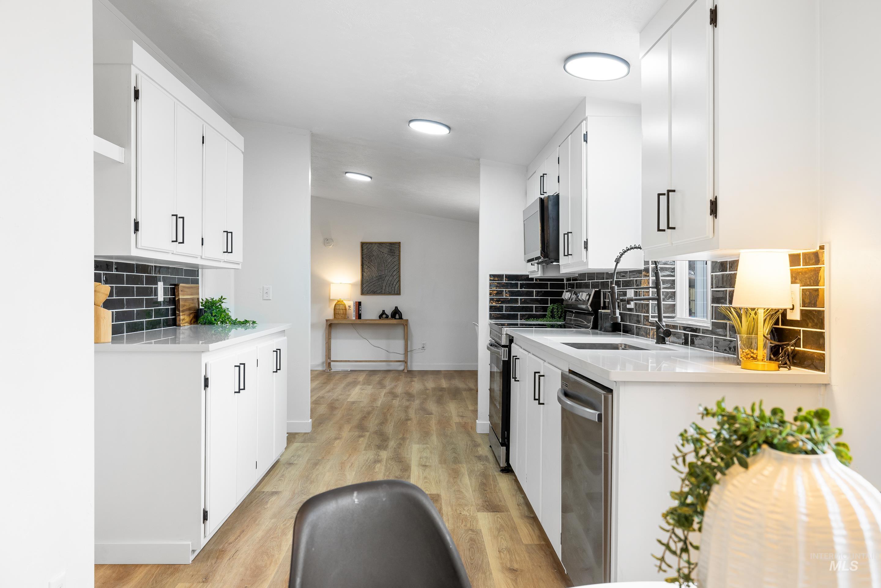 10014 Dewitt Lane Boise, ID 83704 - Photo 26 of 50 Kitchen with decorative backsplash, light stone countertops, white cabinets, appliances with stainless steel finishes, and vaulted ceiling