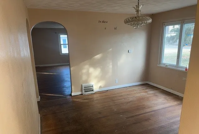 an empty room with chandelier fan and wooden floor