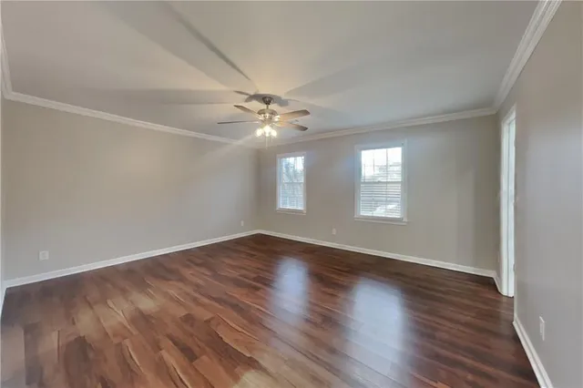 a view of an empty room with wooden floor and fan