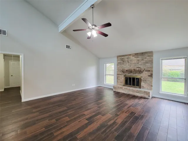 a view of an empty room with wooden floor fireplace and a window