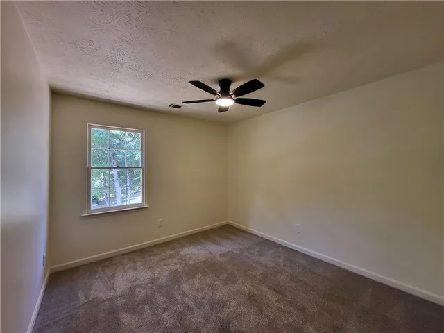 an empty room with chandelier fan and windows