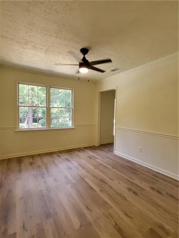an empty room with wooden floor chandelier fan and windows