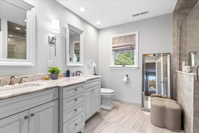 a spacious bathroom with a double vanity sink a large mirror a toilet and a window