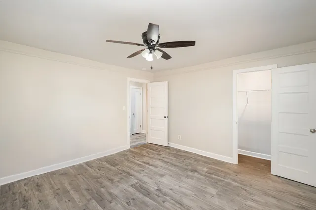 an empty room with wooden floor ceiling fan and windows