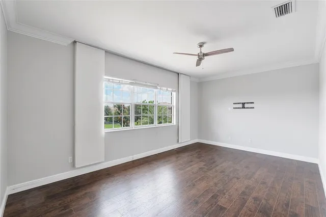 an empty room with wooden floor ceiling fan and windows