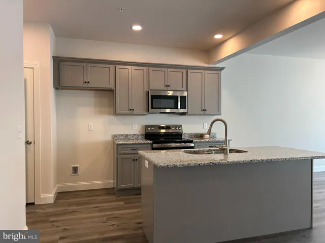 a kitchen with granite countertop a stove top oven a sink dishwasher and a refrigerator with wooden floor