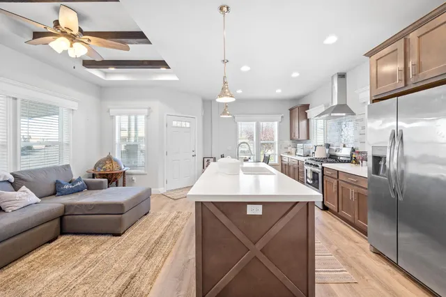 a kitchen with stainless steel appliances kitchen island granite countertop a refrigerator a oven a dining table and chairs with wooden floor