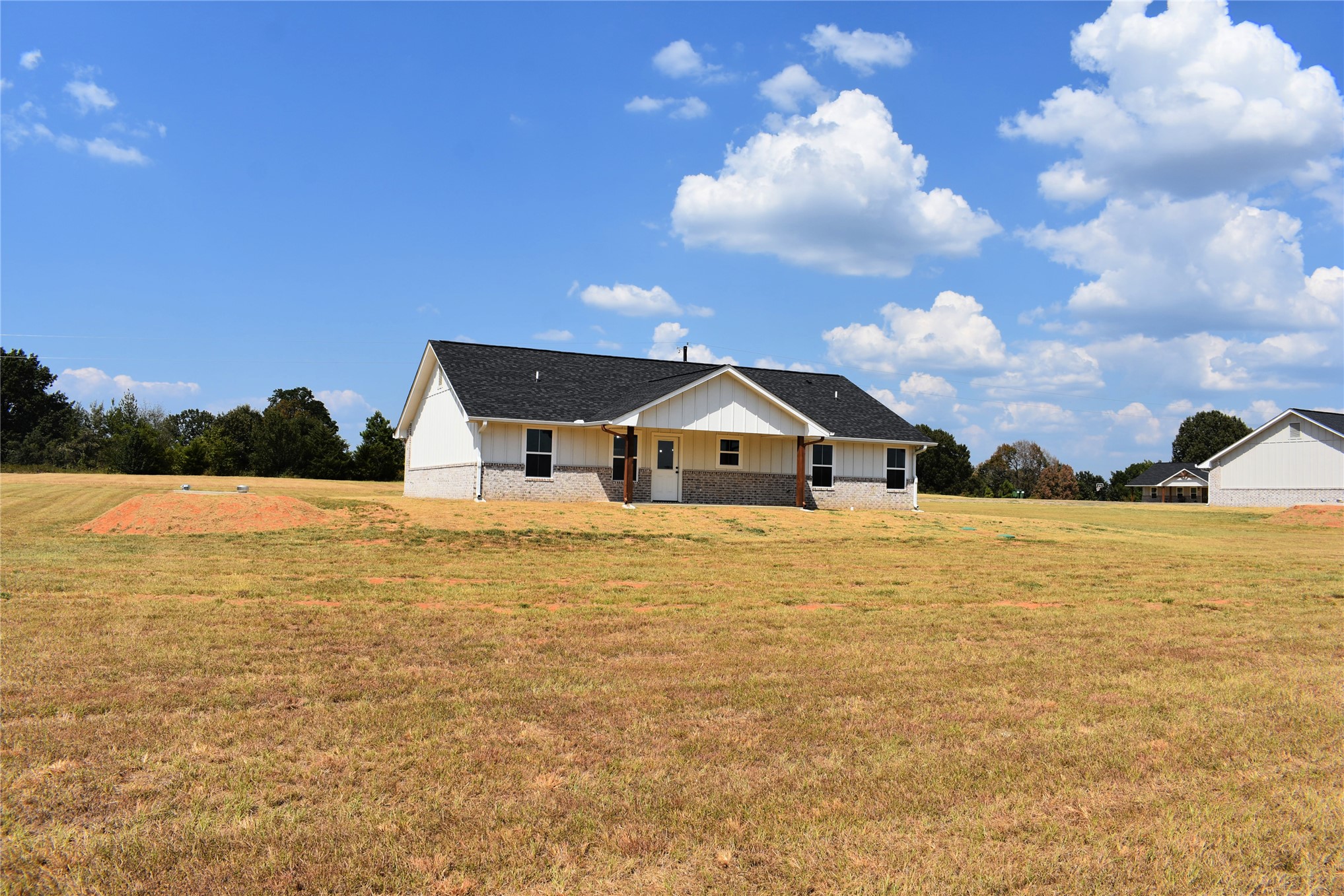 2911 East 2090 Road Hugo, OK 74743 - Photo 22 of 22 Light-colored siding exterior with dark-framed windows, a dark shingled roof, and a partial stone facade