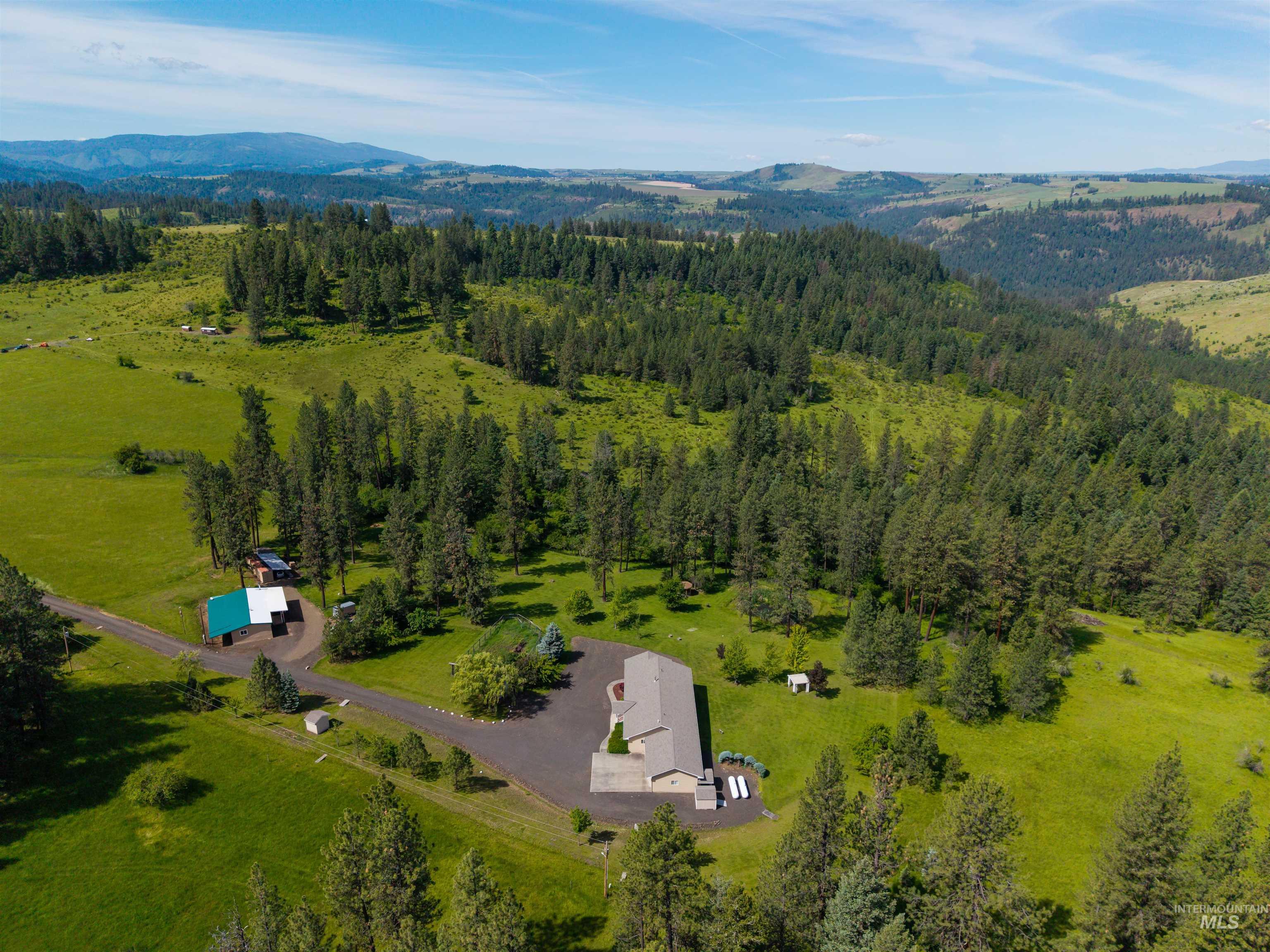 743 Wall Crk Road Stites, ID 83552 - Photo 47 of 48 Expansive property featuring a grey-roofed residence, a green-roofed outbuilding, paved driveways, a large grassy clearing, and extensive evergreen tree coverage
