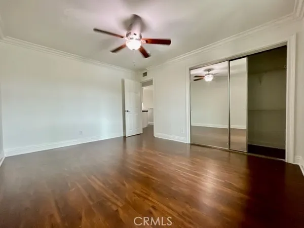 a view of an empty room with wooden floor and a ceiling fan