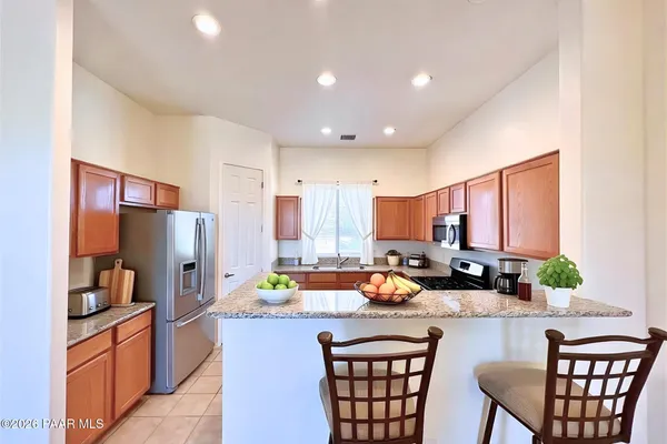 a kitchen with granite countertop a refrigerator a stove a sink and chairs