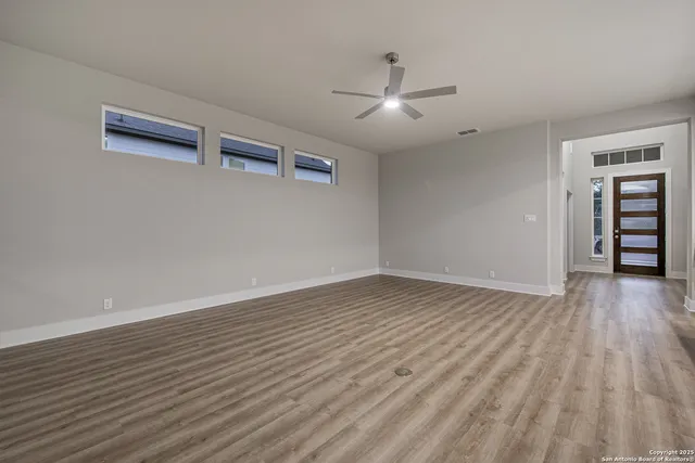 a view of an empty room with wooden floor and a kitchen