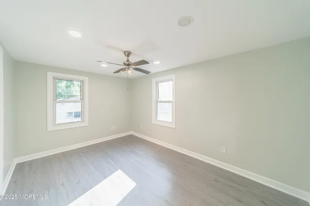an empty room with wooden floor fan and windows