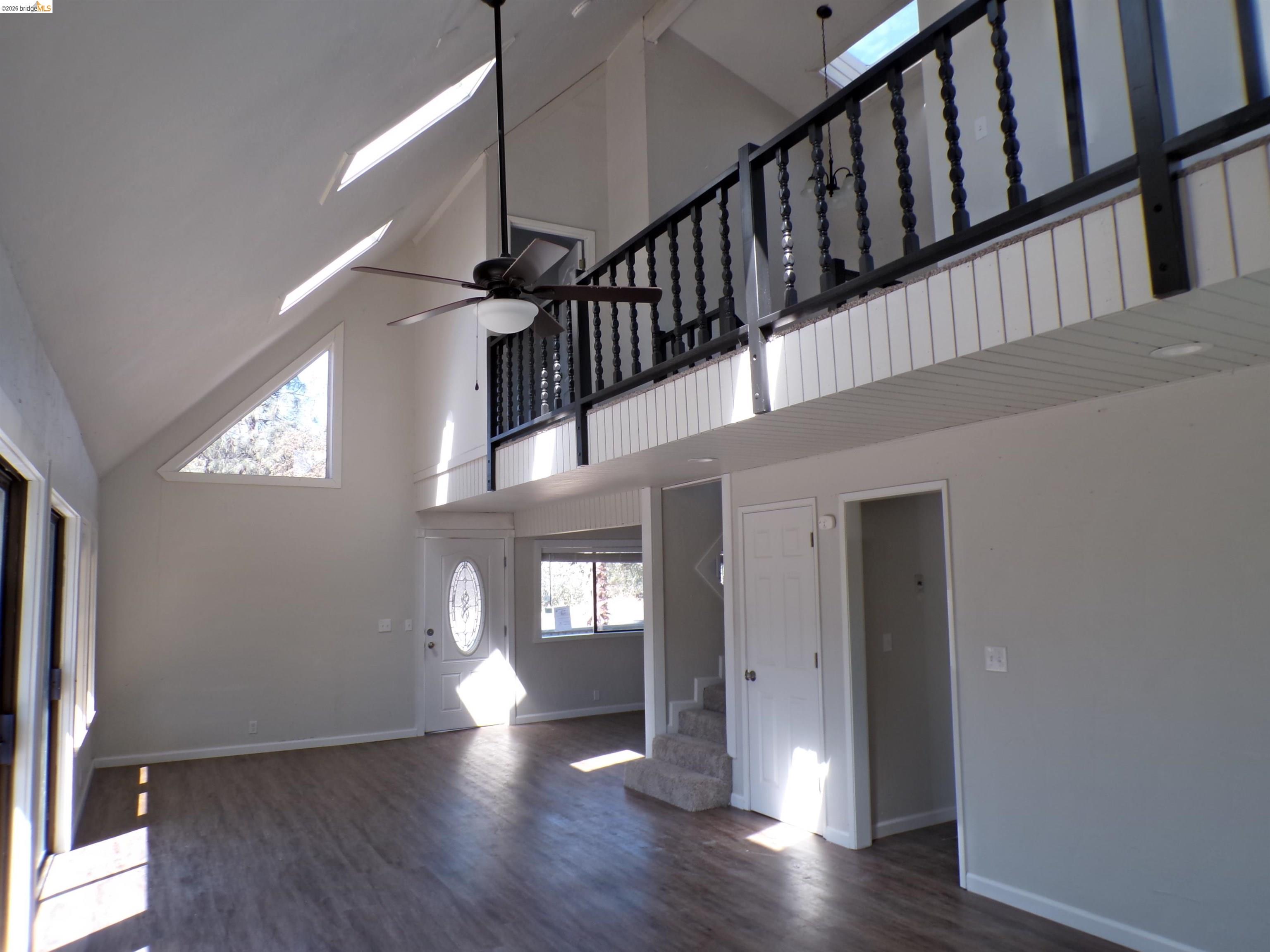 4271 Council Trail Copperopolis, CA 95228 - Photo 12 of 32 Vaulted ceilings with triangular window, wood-finish flooring, open-concept living space, upper-level balcony with black railing, and a decorative glass front door