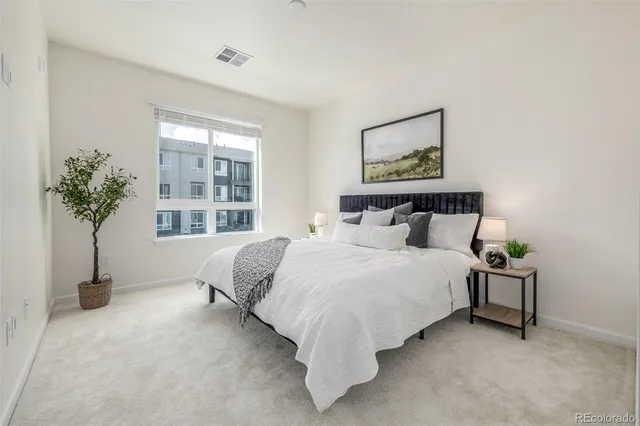 a bed sitting in a spacious bedroom next to a potted plant and a window