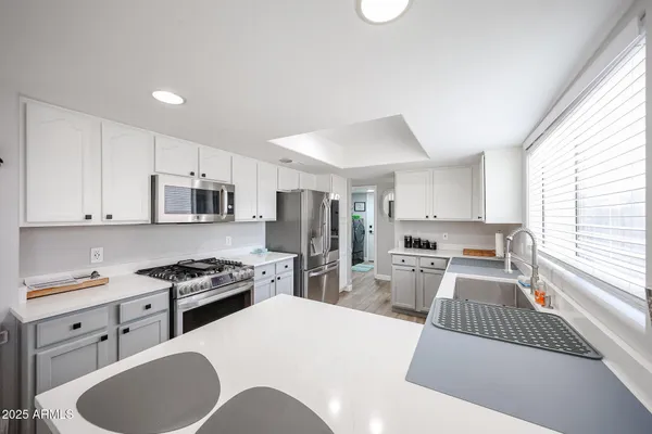 a kitchen with stainless steel appliances kitchen island granite countertop a sink dishwasher stove refrigerator and white cabinets with wooden floor