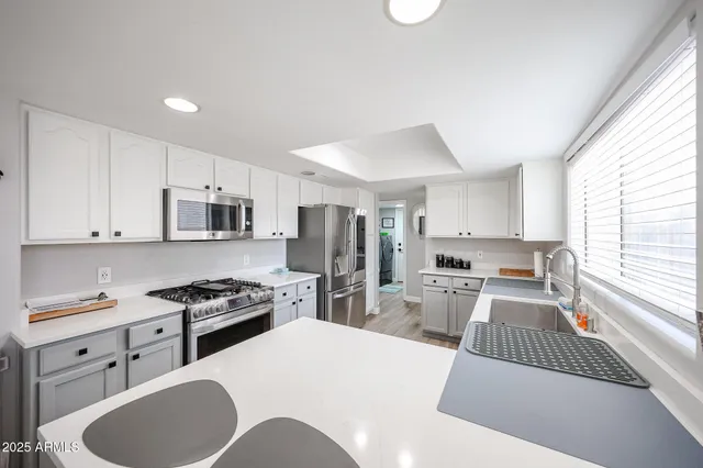 a kitchen with stainless steel appliances kitchen island granite countertop a sink dishwasher stove refrigerator and white cabinets with wooden floor