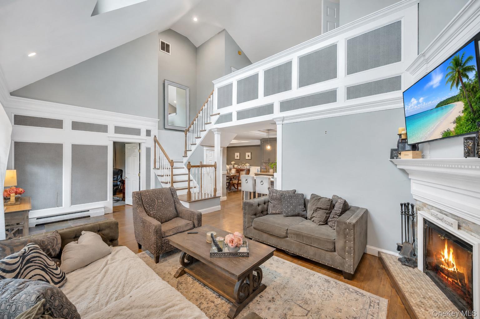 19 Joan Road Bay Shore, NY 11706 - Photo 7 of 50 Two-story living area featuring a vaulted ceiling with skylights, hardwood-finish flooring, a fireplace with a white mantel, and an open staircase with wood railings