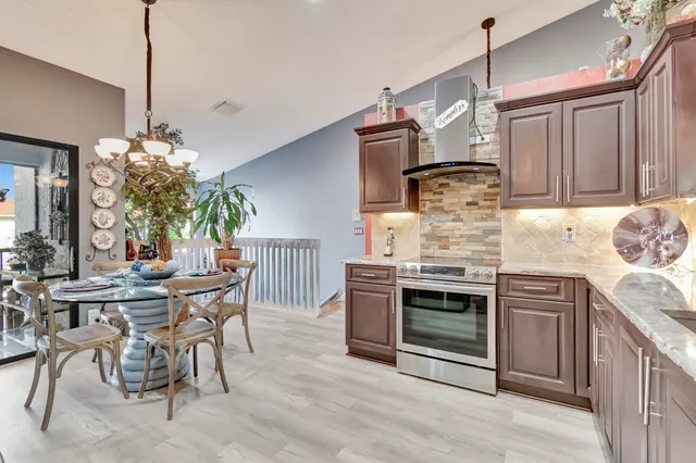 a kitchen with stainless steel appliances granite countertop a stove top oven a sink dishwasher and a dining table with wooden floor