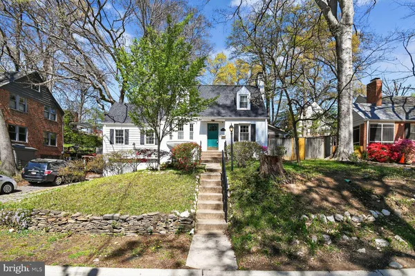 a front view of a house with a yard covered with cars and trees