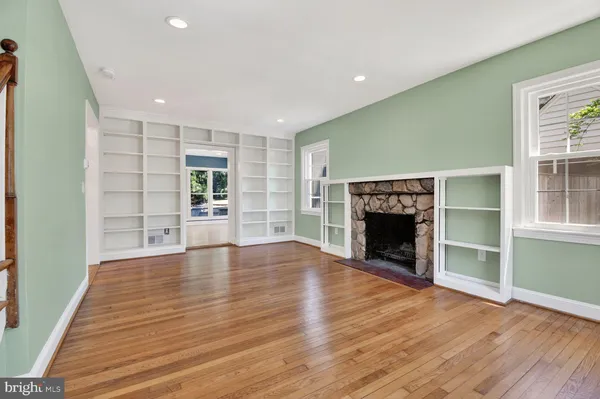 an empty room with wooden floor fireplace and windows
