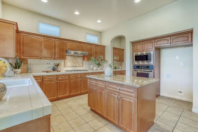 a kitchen with stainless steel appliances kitchen island granite countertop a table chairs sink and cabinets