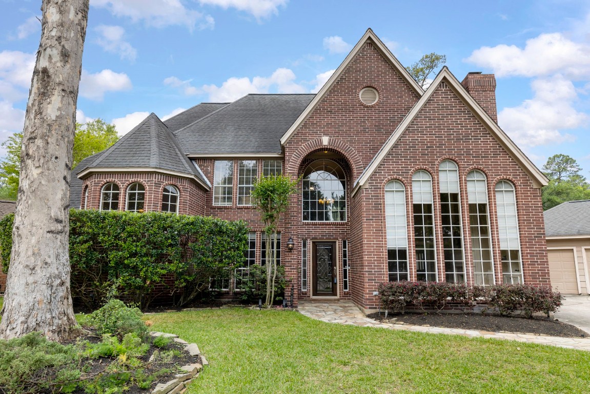 This elegant brick home features a grand facade with tall arched windows, a well-maintained lawn, and mature landscaping, offering plenty of curb appeal.