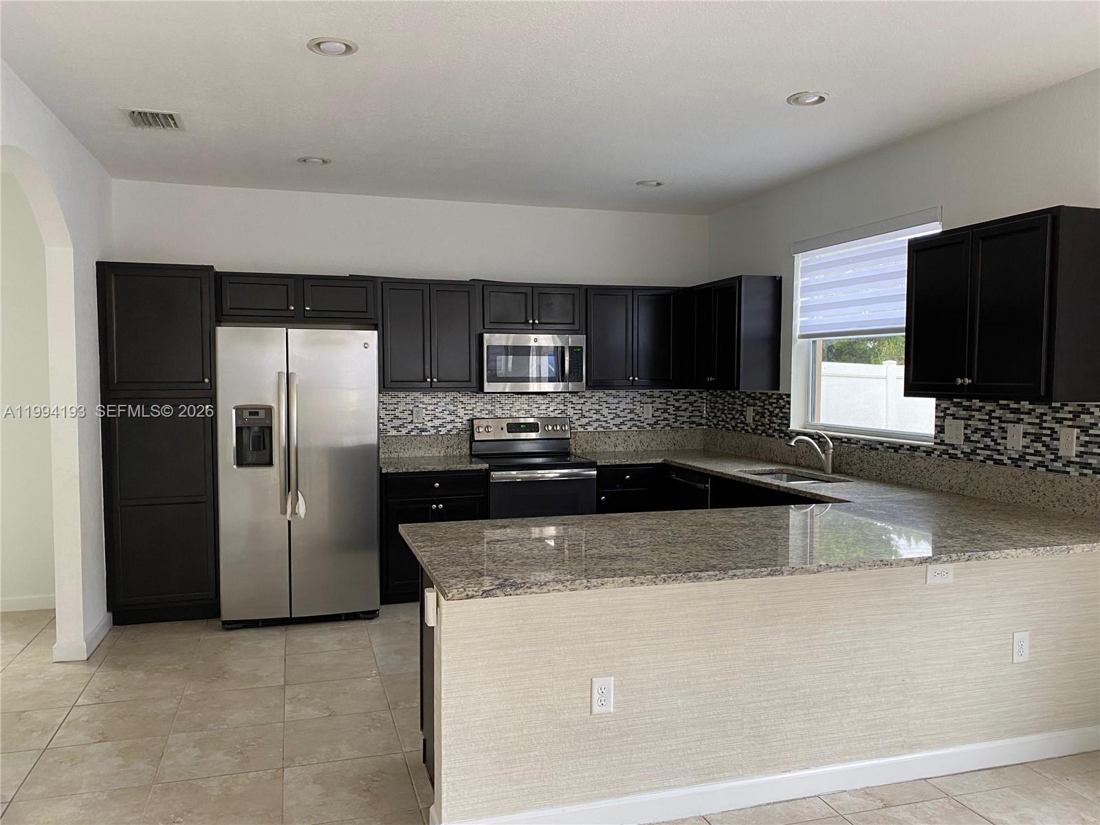 17001 Southwest 90th Terrace, Unit 1 Miami, FL 33196 - Photo 9 of 35 a kitchen with stainless steel appliances granite countertop a refrigerator a stove a sink and a microwave
