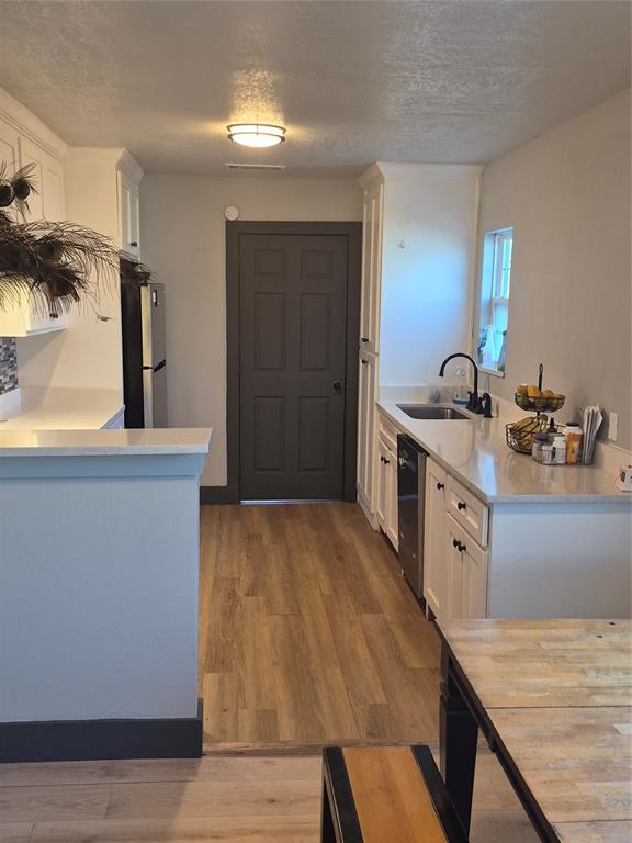 815 Bonnie View Road Dallas, TX 75203 - Photo 6 of 29 Kitchen featuring a peninsula, white cabinets, a textured ceiling, light wood-style floors, and stainless steel appliances