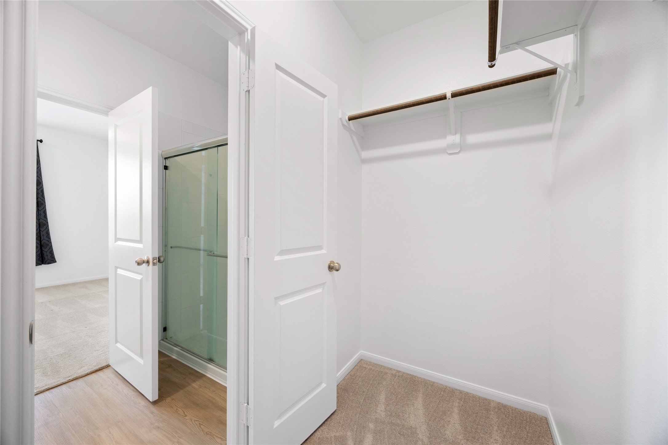 17907 Grain Auger Road Hockley, TX 77447 - Photo 23 of 24 carpeted walk-in closet with a wooden rod for hanging clothes. It connects to a room with wood flooring and a glass-enclosed shower. The area is bright and well-maintained.