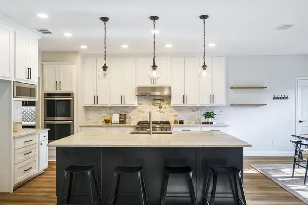 a kitchen with stainless steel appliances kitchen island granite countertop a table chairs in it and white cabinets