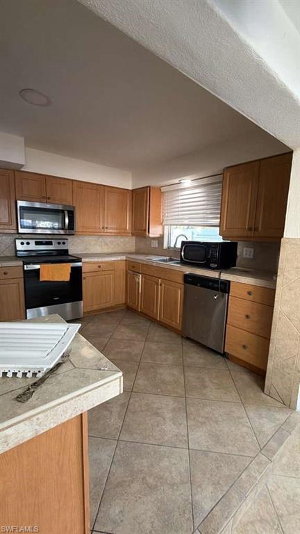 4439 23rd Place Southwest Naples, FL 34116 - Photo 7 of 15 Kitchen featuring appliances with stainless steel finishes, brown cabinetry, light countertops, and light tile patterned floors