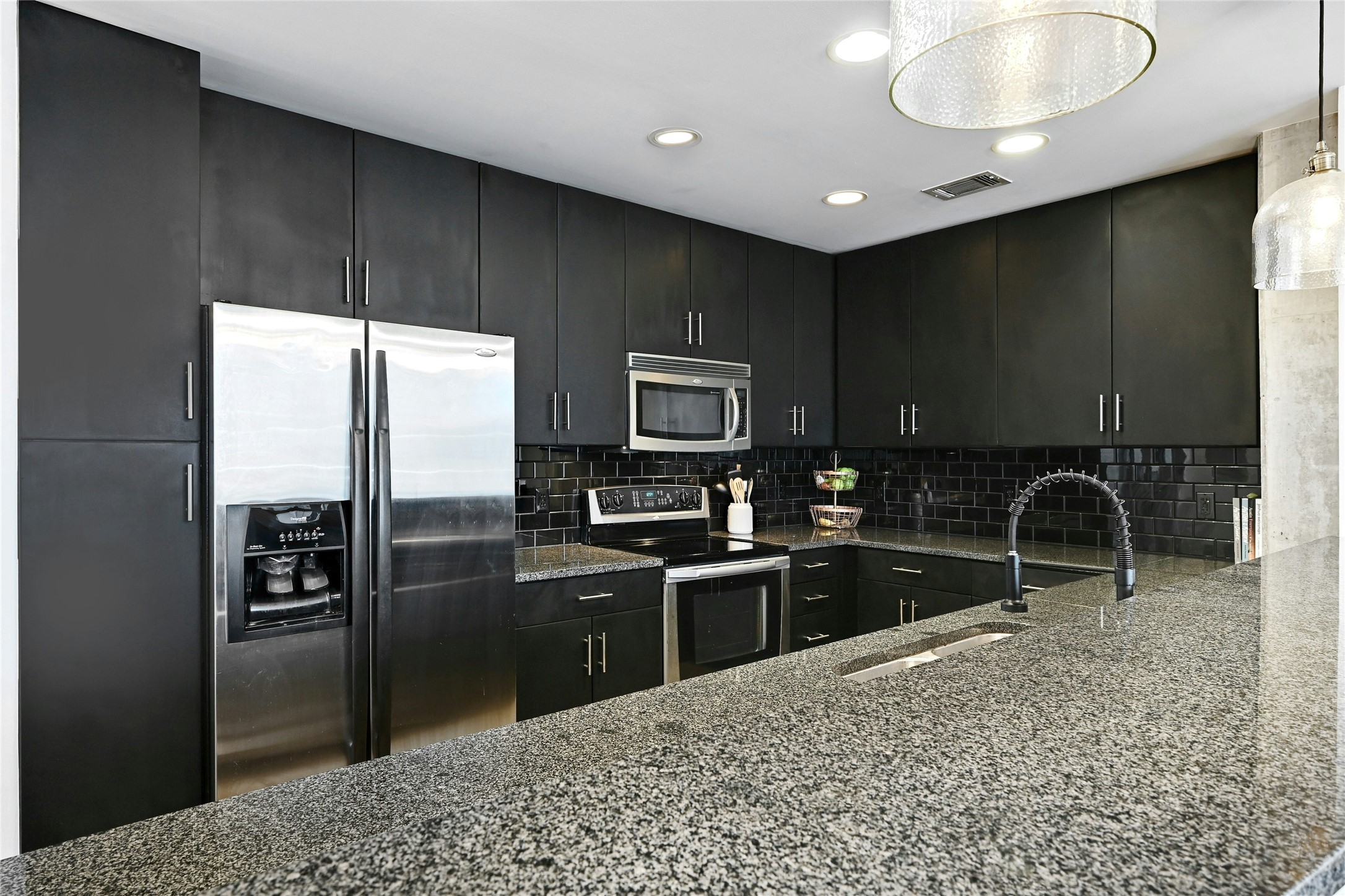 360 Nueces Street, Unit 1809 Austin, TX 78701 - Photo 11 of 25 Kitchen featuring stainless steel appliances, light stone counters, dark cabinetry, a peninsula, and backsplash