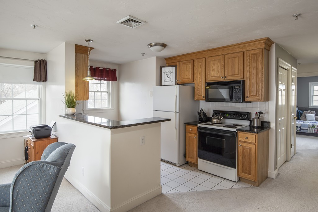 24 Wall Street, Unit E Canton, MA 02021 - Photo 5 of 19 a kitchen with stainless steel appliances granite countertop a stove top oven a sink dishwasher a dining table and chairs with wooden floor
