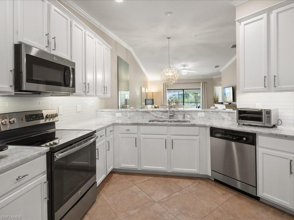 9532 Avellino Way, Unit 2726 Naples, FL 34113 - Photo 8 of 35 Kitchen featuring stainless steel appliances, backsplash, white cabinetry, and ornamental molding